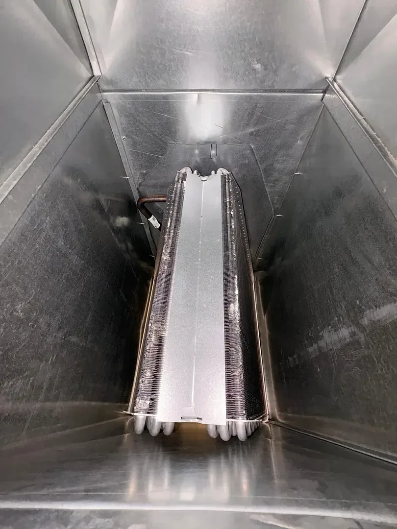 Looking down at an A-frame AC coil inside the metal casing above a furnace