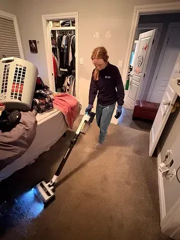 Rachel cleaning carpet alongside a bed in a home